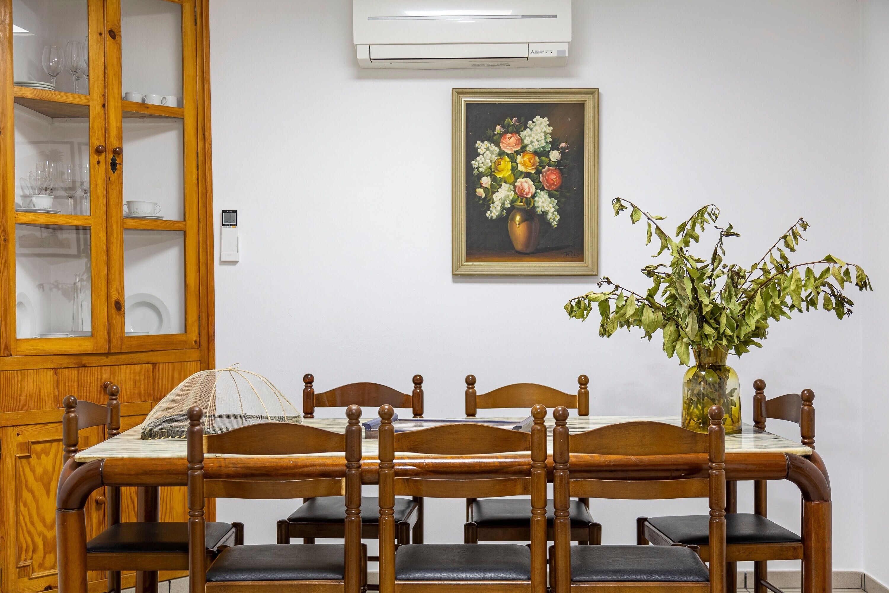 A dining area with a wooden table, chairs, a glass cabinet, and a painting on the wall.