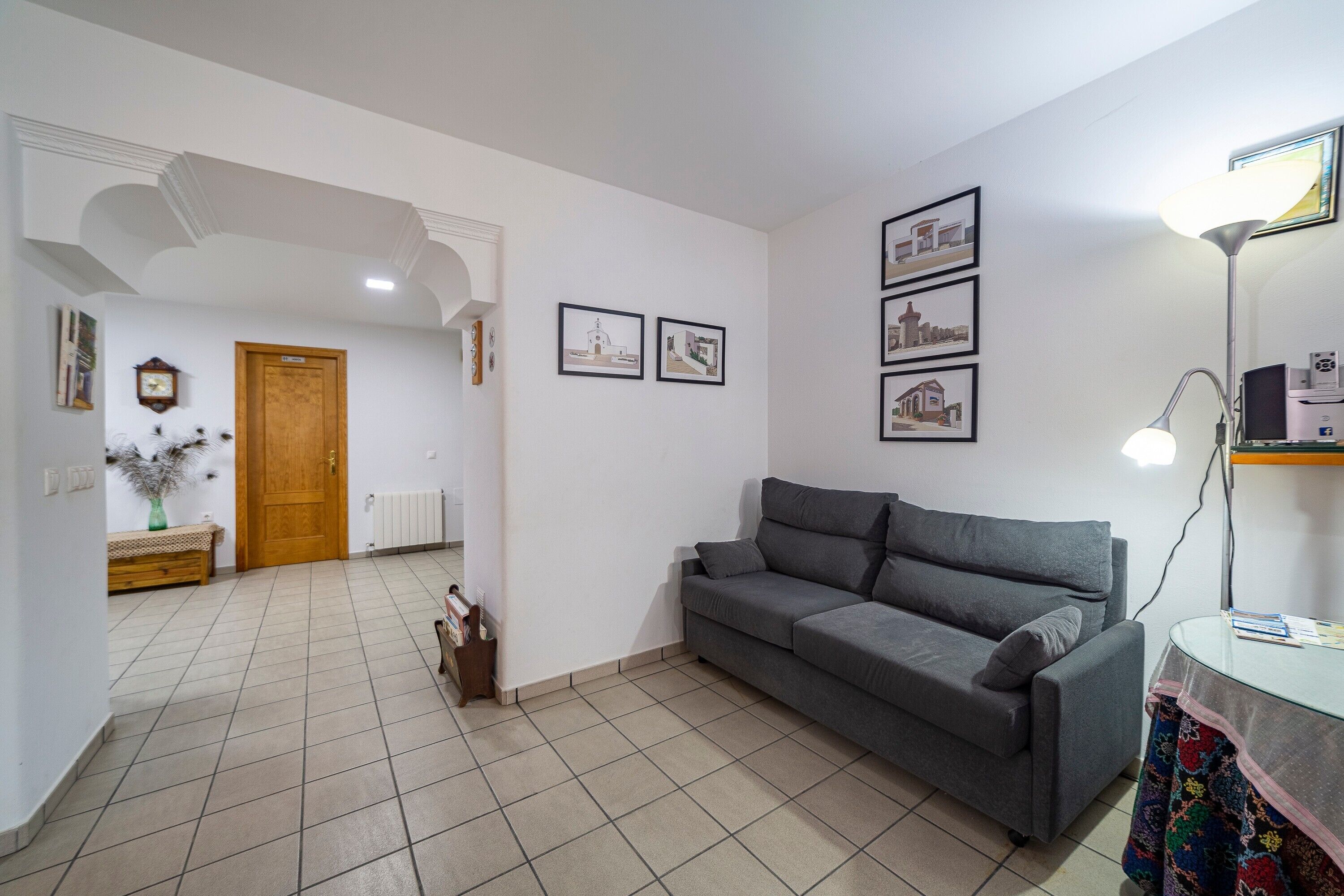 Un salón con sofá gris, puerta de madera, radiador y cuadros en la pared.