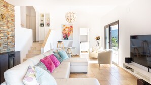 En moderne stue med sofa, TV og trappe op til spiseområde.