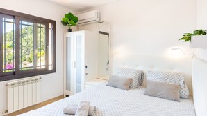 Et soveværelse med seng, radiator, garderobeskab og et vindue med udsigt over grønne omgivelser.