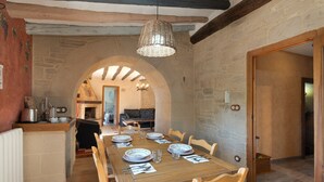 Un coin repas avec une table en bois dressée pour quatre personnes, des murs en pierre et un luminaire suspendu.