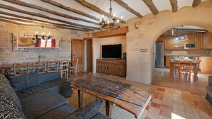 Un intérieur rustique avec des poutres apparentes, un mur en pierre, un téléviseur et un coin repas.