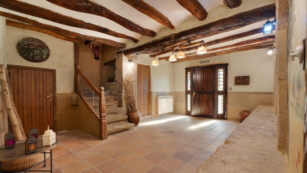 Un intérieur rustique avec des poutres apparentes, un escalier, un coin repas avec une table et des chaises, et un panneau indiquant la « SORTIE ».