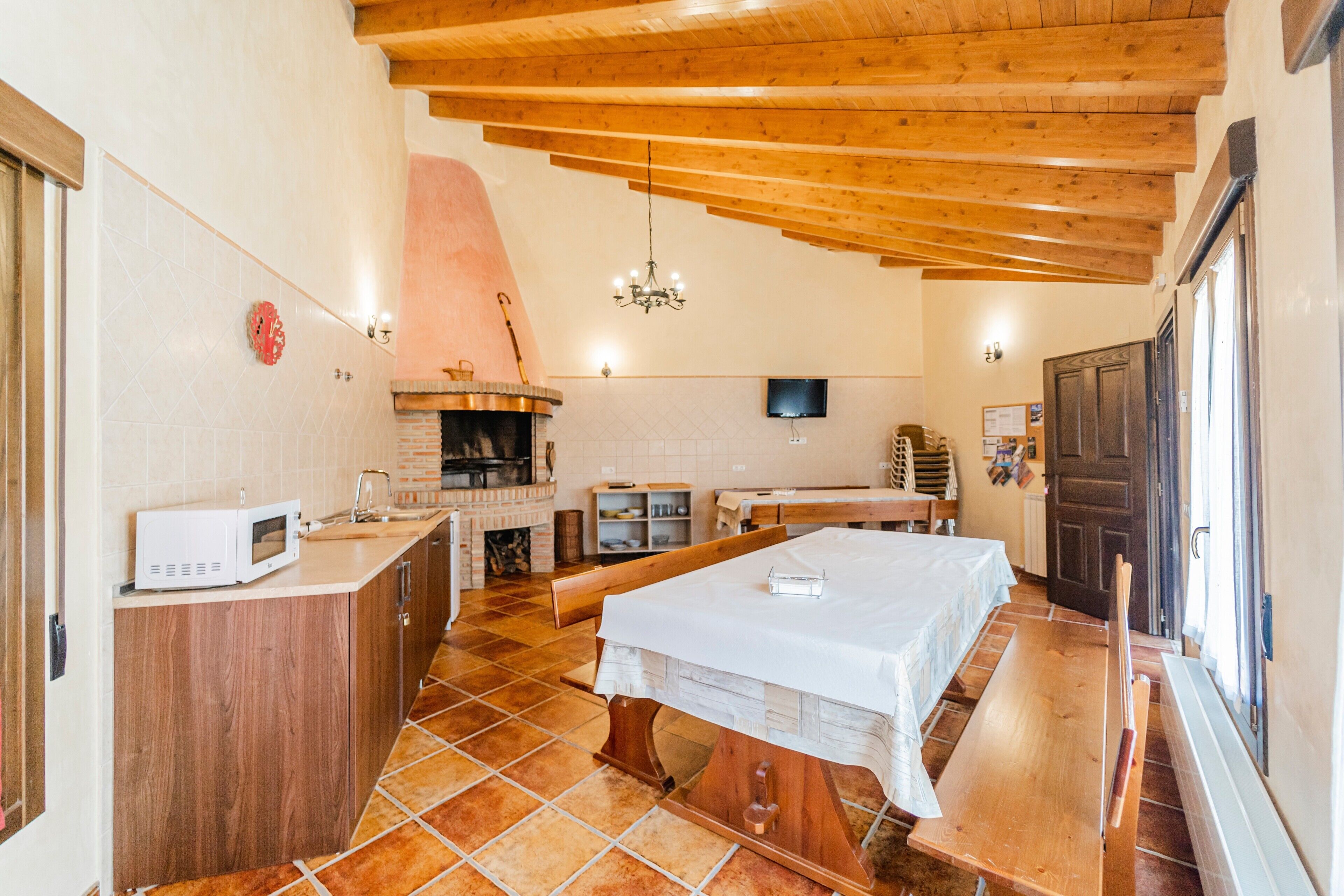 Una cocina con microondas, armarios de madera, un horno de ladrillo y una mesa con bancos.