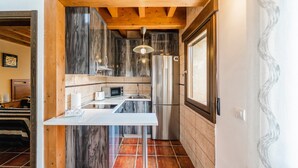 Une cuisine compacte dotée d’un plan de travail blanc, d’appareils électroménagers en acier inoxydable et d’un plafond en bois.