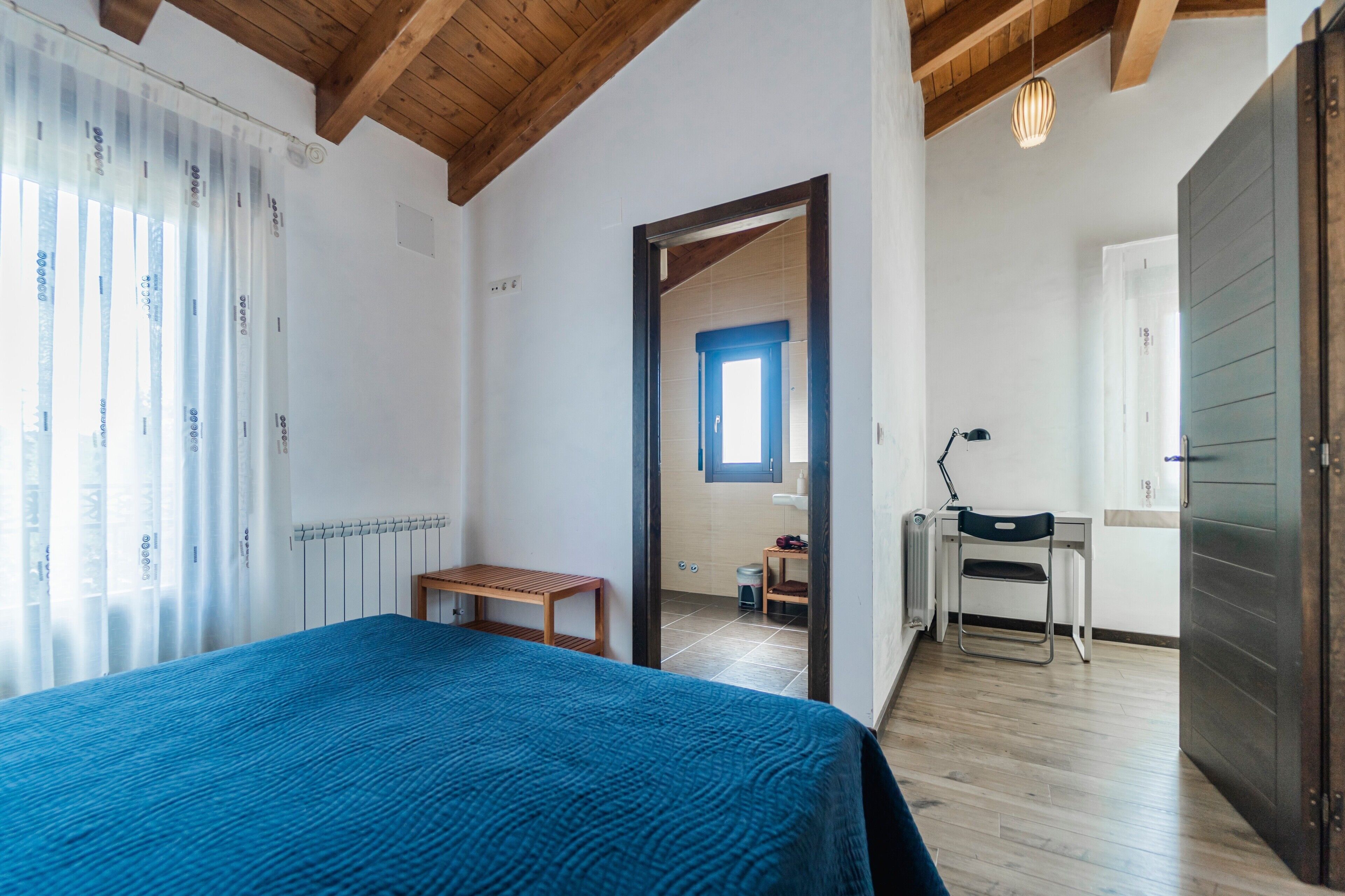 A bedroom with a bed, a wooden bench, a desk, and a chair.