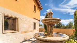 Une fontaine en pierre se trouve devant un bâtiment doté d’une fenêtre, et le ciel est dégagé.
