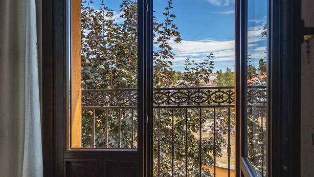 Un balcon orné d’une balustrade en fer forgé, avec vue sur les arbres et un ciel dégagé.