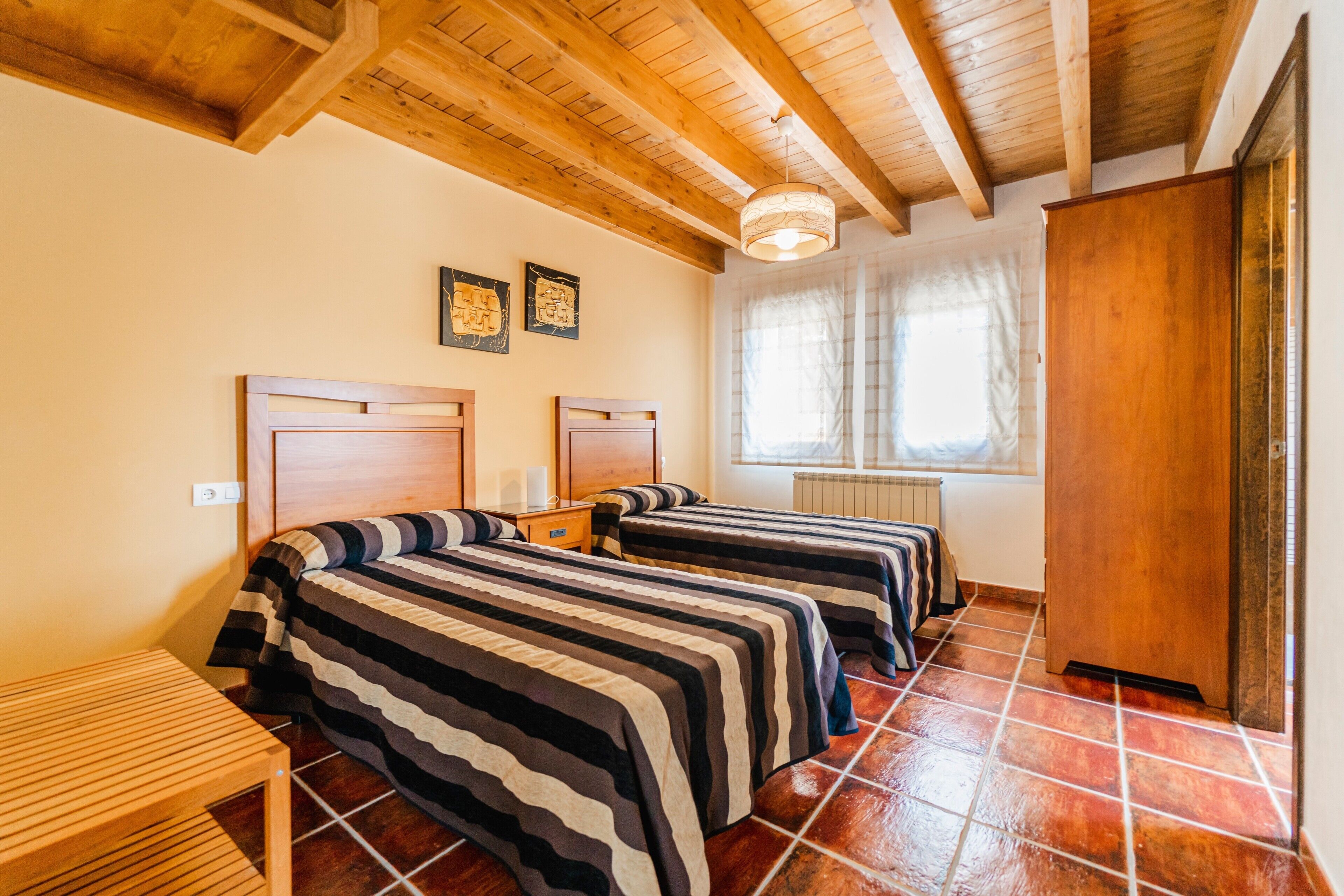 Una stanza con due letti, travi in legno al soffitto, un termosifone e una finestra con tende.