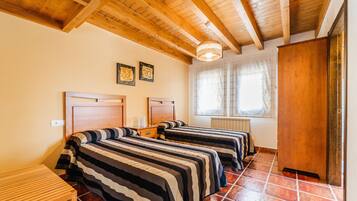 Una stanza con due letti, travi in legno al soffitto, un termosifone e una finestra con tende.