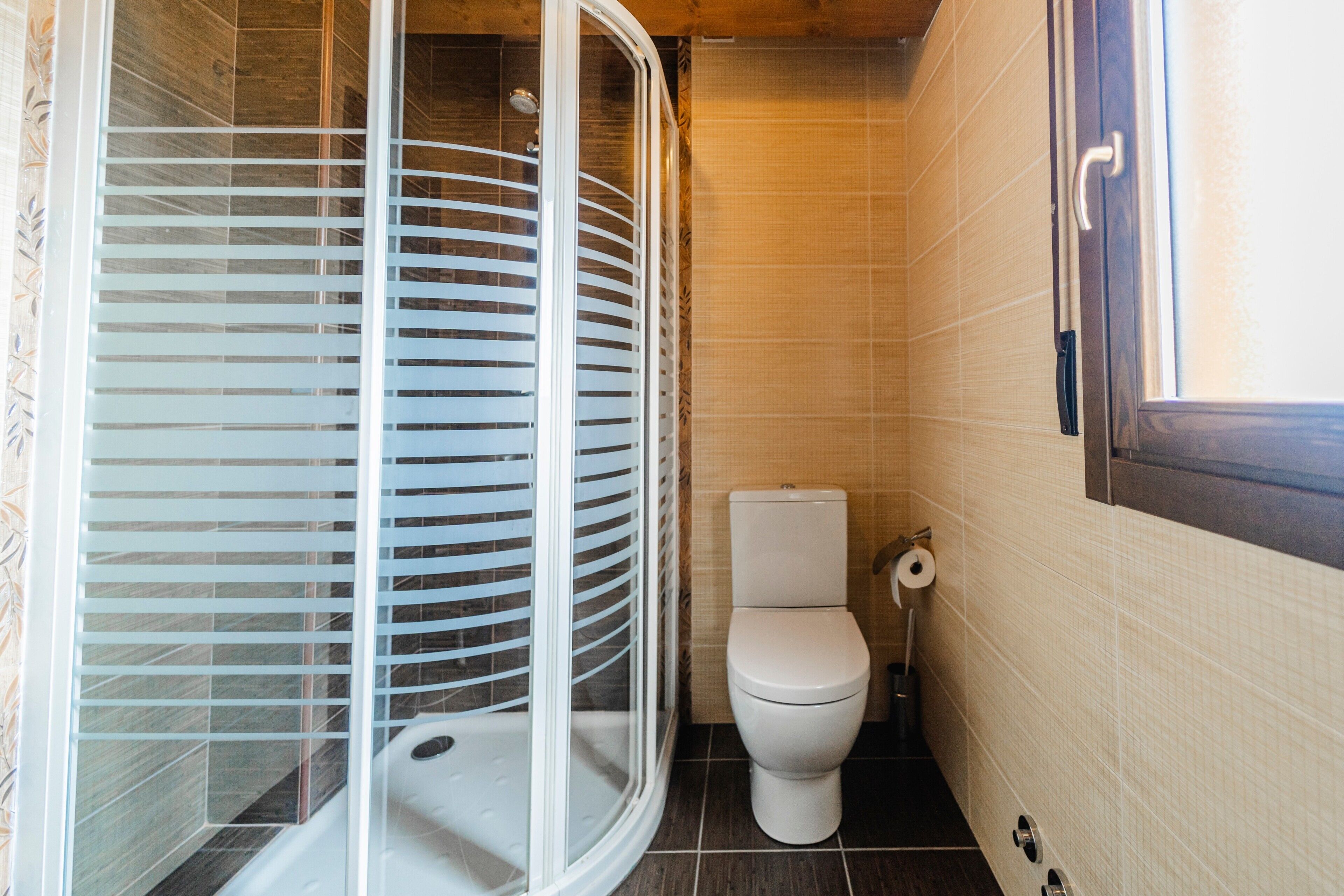 A bathroom with a shower enclosure, toilet, and tiled walls.