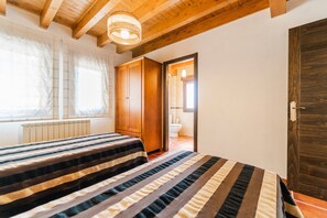 Une chambre avec un plafond en bois, un lit avec une literie à rayures, un radiateur et une porte donnant sur une salle de bain.