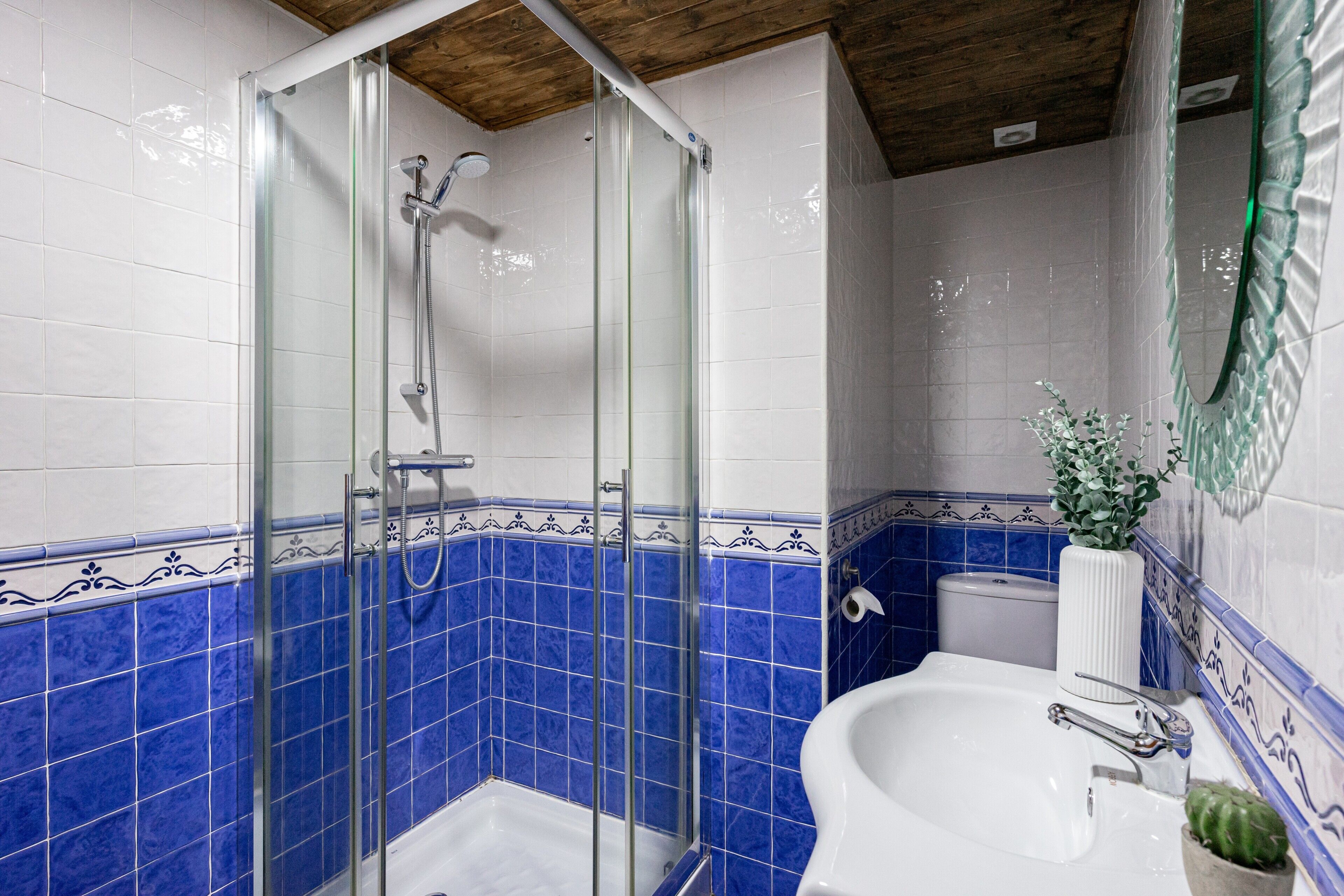 A bathroom with a glass-enclosed shower, a white sink, and blue-tiled walls.