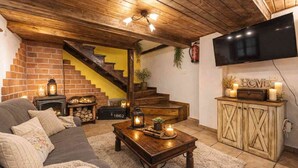 Ein gemütliches Wohnzimmer mit Kamin, einer Couch, einem Couchtisch mit Kerzen, einer Treppe und einem an der Wand befestigten Fernseher.