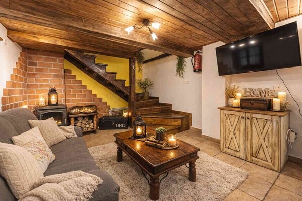 A cozy living room with a fireplace, a sofa, a coffee table with candles, a staircase, and a TV mounted on the wall.