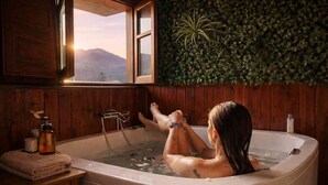 Eine Person entspannt in einer Badewanne mit Blick auf Berge durch ein Fenster.