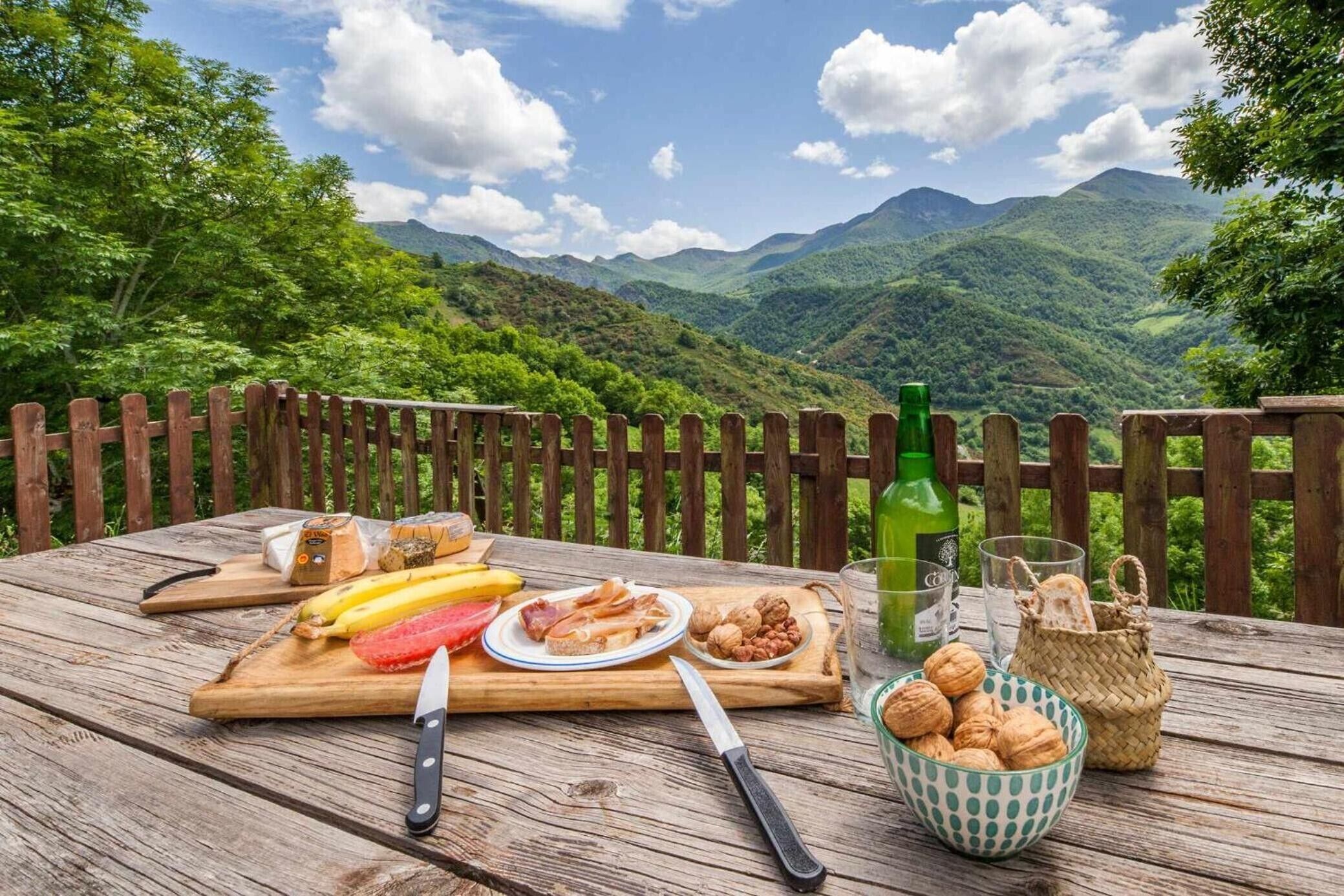 Une table en bois avec de la nourriture et des boissons, une clôture en bois et, en arrière-plan, un paysage montagneux.