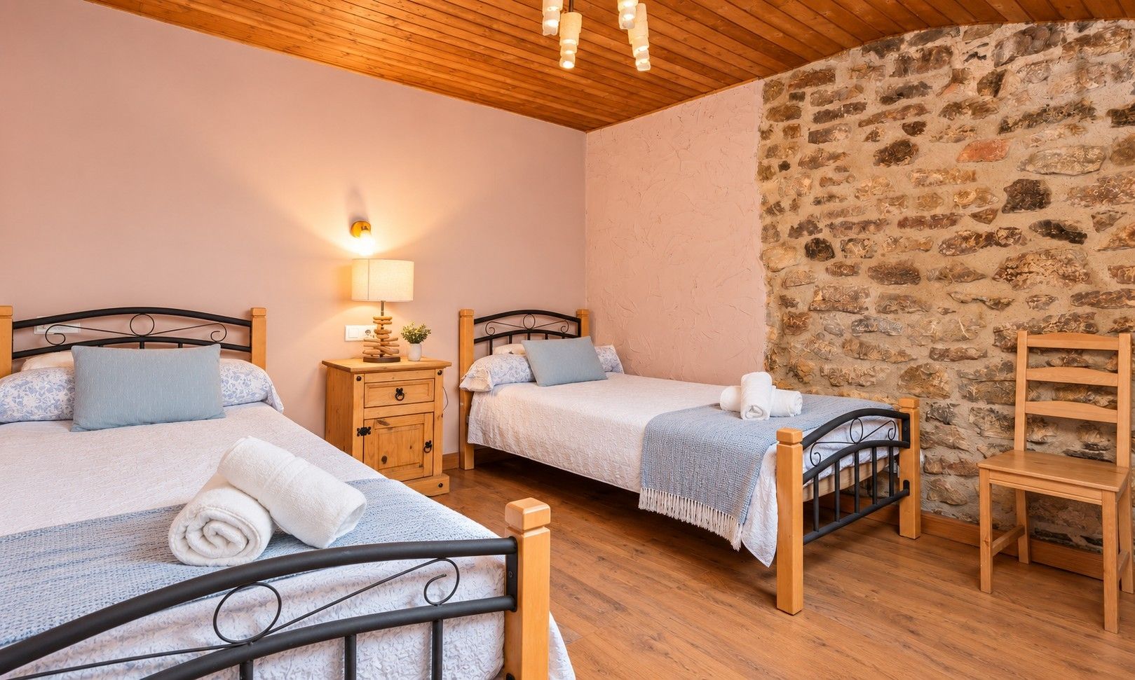 Ein Zimmer mit zwei Einzelbetten, Holznachttischen, einer Steinwand und einer Holzbalkendecke.