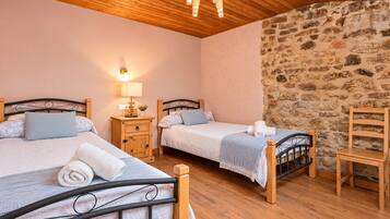 Ein Zimmer mit zwei Einzelbetten, Holznachttischen, einer Steinwand und einer Holzbalkendecke.