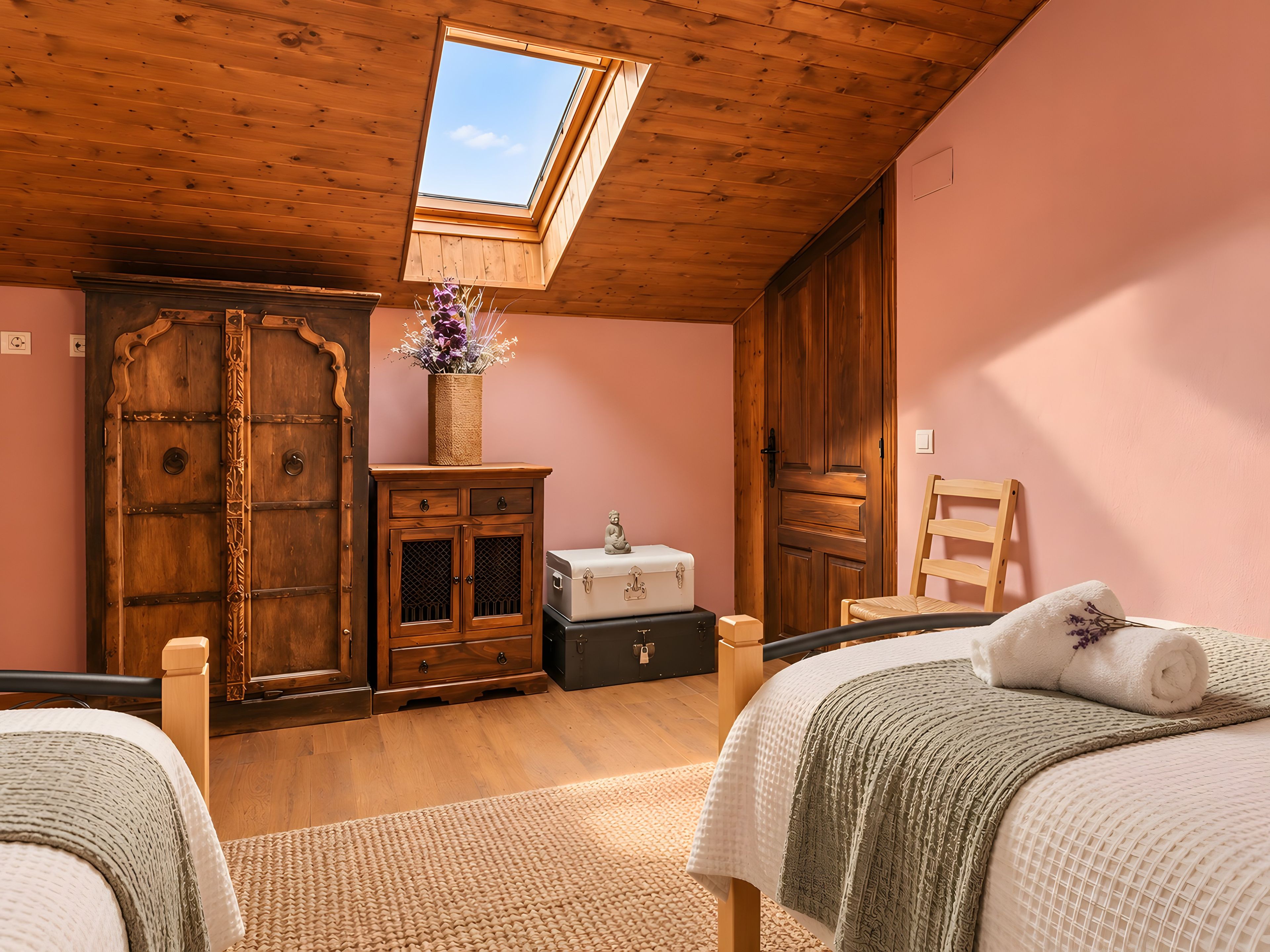 A bedroom with a skylight, wooden wardrobe, and a bed with a rolled towel.