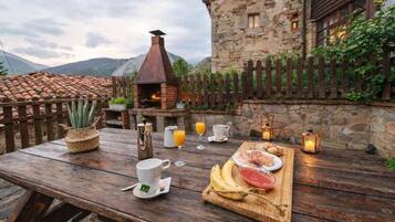Un'area pranzo esterna rustica con un edificio in pietra, una recinzione in legno e un forno a mattoni.