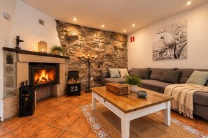 A cozy living room with a stone wall, a fireplace, a sofa, and a coffee table. - Apartment 'El Ablanu, Hot Tub & Mountain Views' with Terrace and Wi-Fi (Proaza)