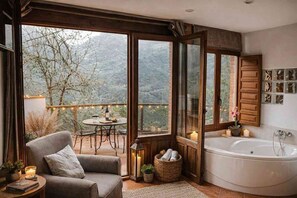 Ein gemütliches Zimmer mit großem Fenster, einer Badewanne, einem Sofa und einem kleinen Tisch mit Kerzen.