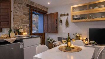 Une cuisine avec des murs en pierre, des meubles en bois, une table à manger décorée de bougies et un téléviseur.