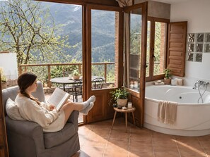 A woman reading on a sofa with a view of mountains through a glass door. - Apartment 'El Ablanu, Hot Tub & Mountain Views' with Terrace and Wi-Fi (Proaza)