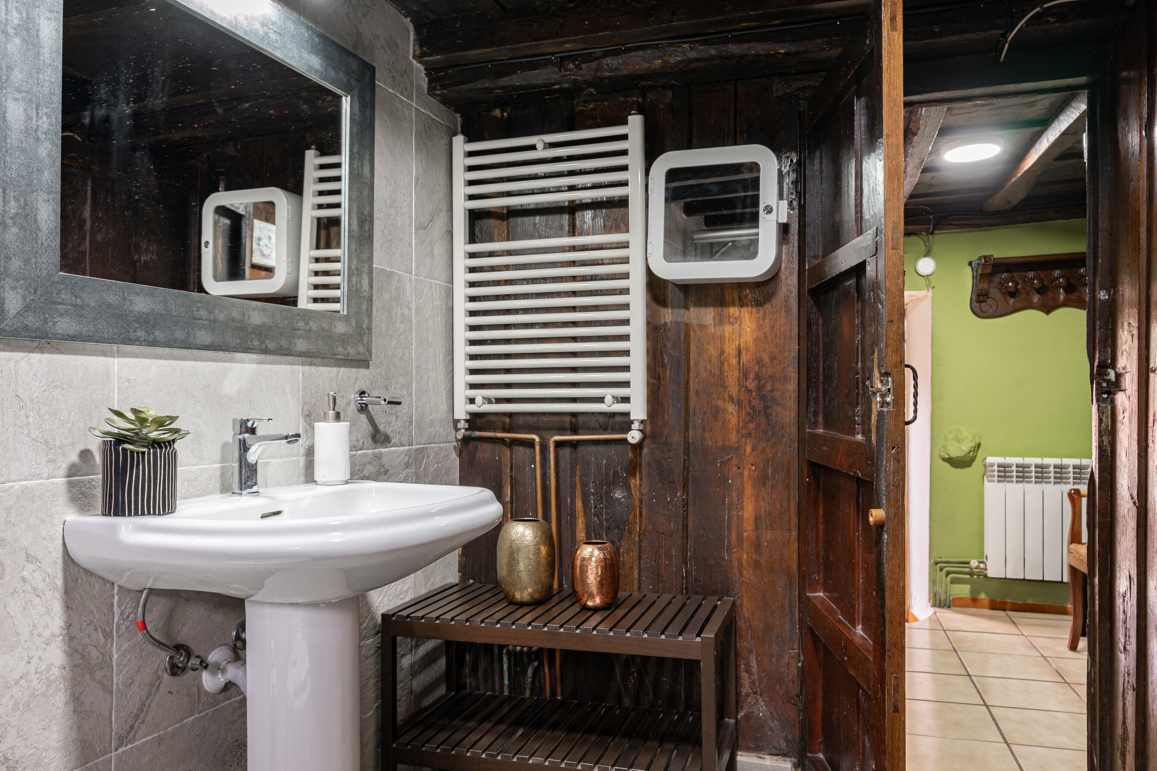 Un baño con un lavamanos blanco, un espejo, un perchero para toallas y un radiador.