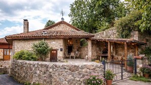 Un edificio de piedra con techo de tejas, un área de estar al aire libre techada y un muro de piedra que rodea la propiedad.