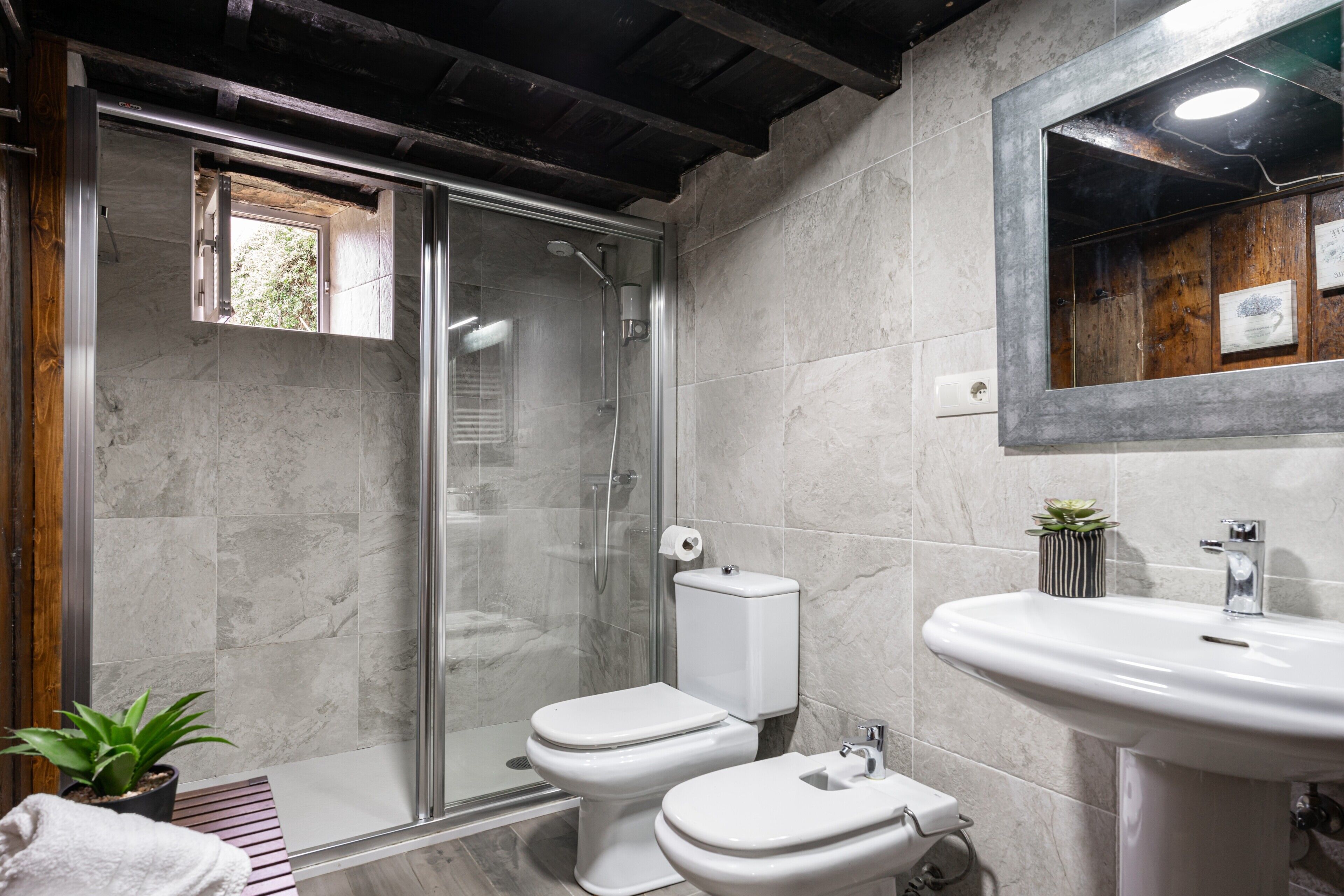 A bathroom with a glass-enclosed shower, two toilets, a sink, and a mirror.