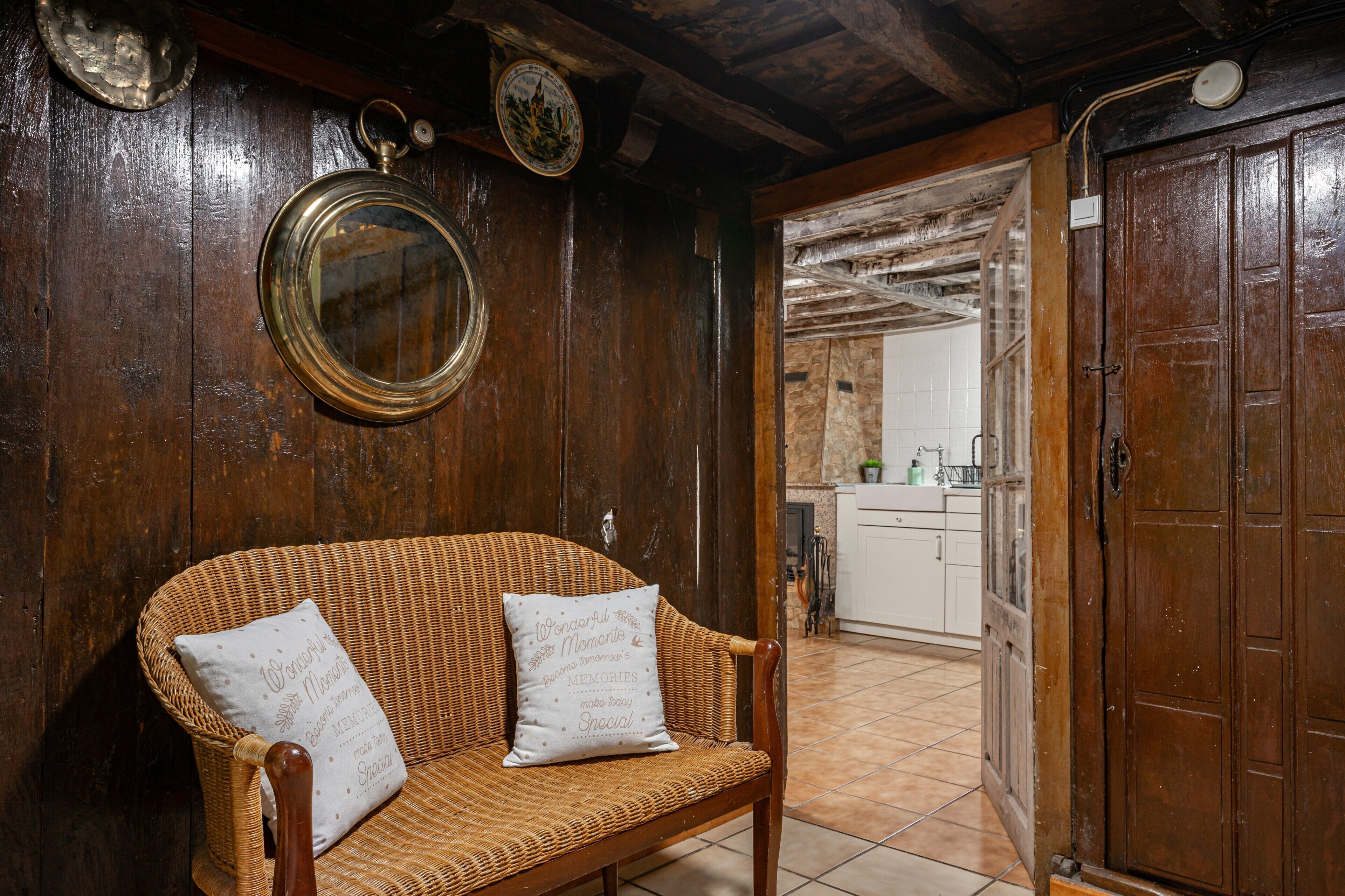 Un canapé en osier avec deux coussins, un miroir rond et une porte en bois, le tout dans un décor rustique.