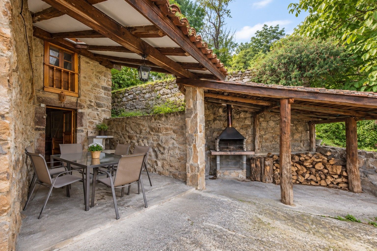 Un edificio de piedra con un patio cubierto, una mesa con sillas y un horno de leña.