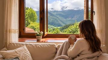 A person sitting on a sofa by a window with a view of a mountainous landscape.