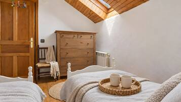 Une chambre avec un plafond en pente, des meubles en bois, un lit avec une tête de lit blanche, une commode en bois et une petite fenêtre.