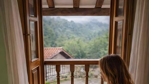 Una persona sentada junto a una ventana con vista a un área boscosa, sosteniendo una taza.