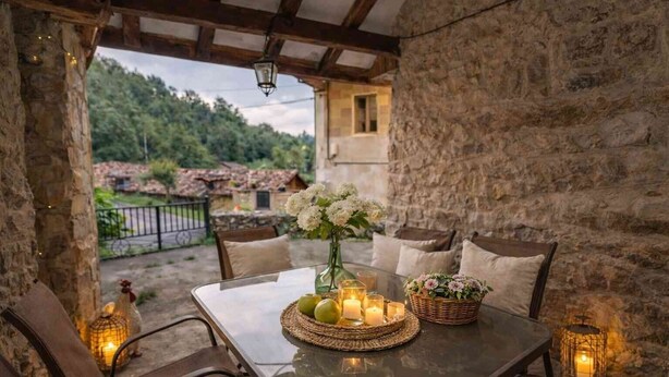 Un espacio al aire libre con paredes de piedra, una mesa dispuesta para dos personas, velas y un florero con flores.
