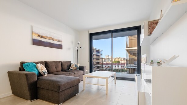 Un salon moderne avec un canapé, une table basse et une vue sur les immeubles à travers une grande porte vitrée.