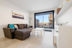 Un salon moderne avec un canapé, une table basse et une vue sur les immeubles à travers une grande porte vitrée.