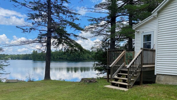 A lakeside cabin with a wooden deck and a staircase leading to a window.