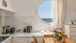 A kitchen with a view of the sea, a toaster, a kettle, and a basket of groceries.
