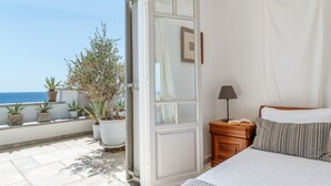 A bedroom with a bed, bedside table, lamp, and a view of the sea.