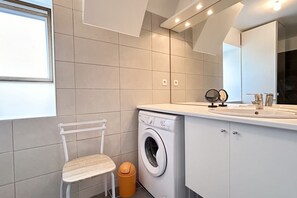 A modern bathroom with a washing machine, a sink, and a mirror.