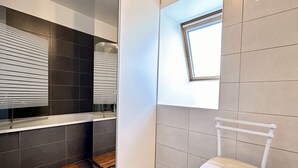Un baño moderno con ducha, una ventana pequeña y una silla blanca.