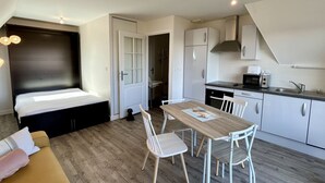 Habitación pequeña con cama, una mesa de comedor con sillas, kitchenette y un perro.
