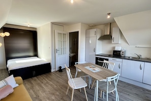 Habitación pequeña con cama, una mesa de comedor con sillas, kitchenette y un perro.