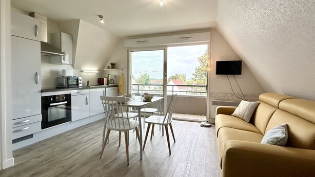 Una cocina moderna con armarios blancos, una mesa de comedor con sillas, un sofá y un televisor montado en la pared.