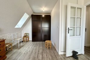 A room with a sloped ceiling, a dark wardrobe, a white door, and a small stool.
