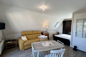 A compact living space with a sofa, a small dining table, a bed, and a television.